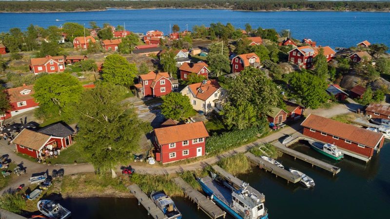 Aerial view of a lakeside village with red houses and boats docked at piers.