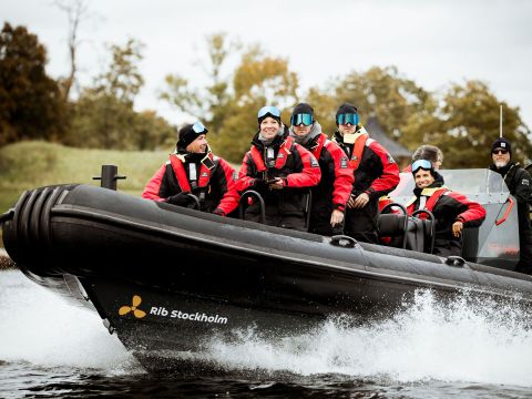 Group in red jackets on speedboat marked 'Rib Stockholm' riding through water.