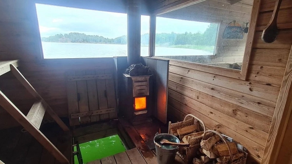 Interior of a wooden sauna with a stove, overlooking a lake through a window.