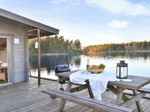 Lakeside cabin deck with picnic table, food, wine, and a grill.