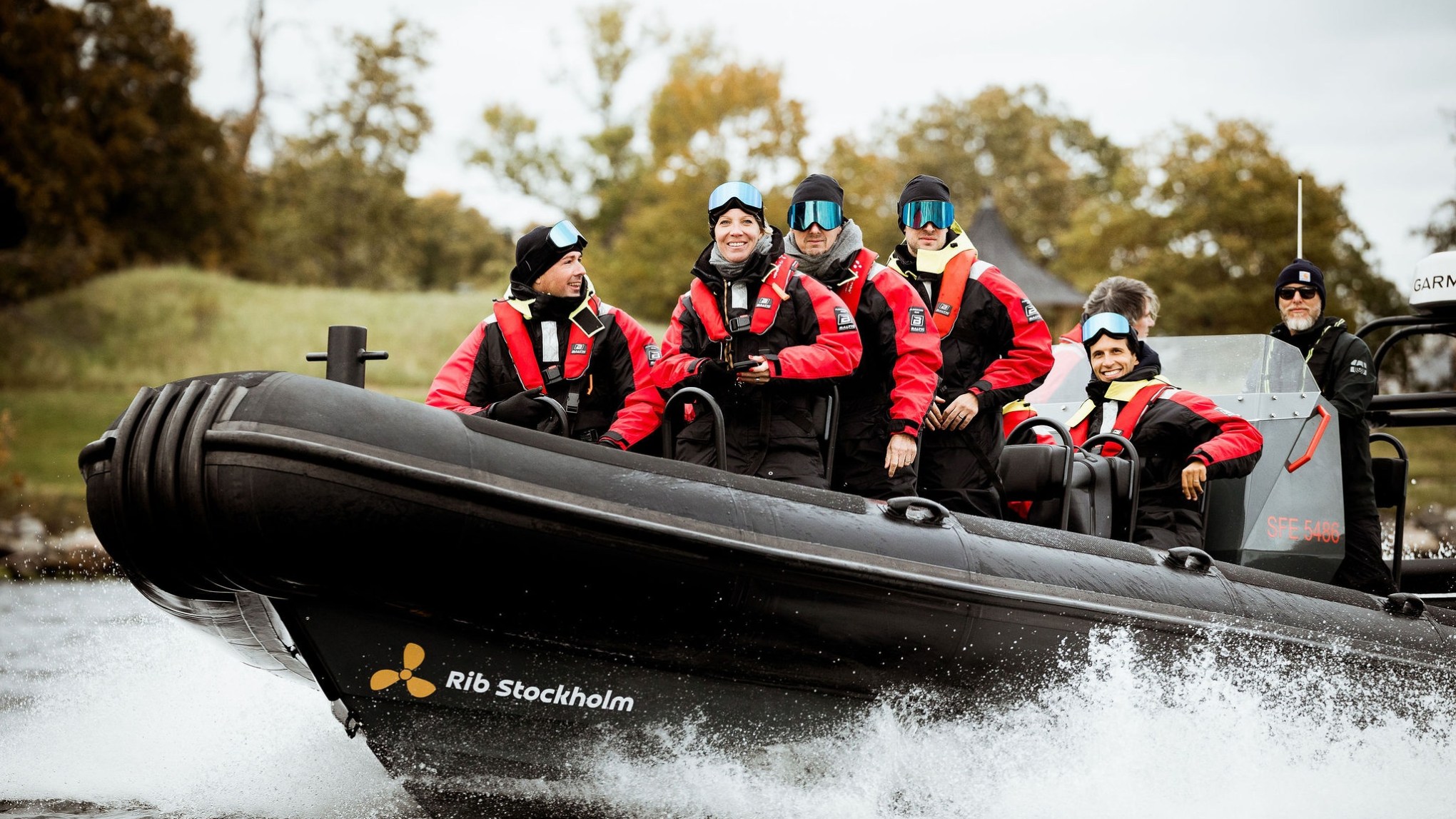 Group wearing red life jackets on a speedboat in motion, with trees in the background.