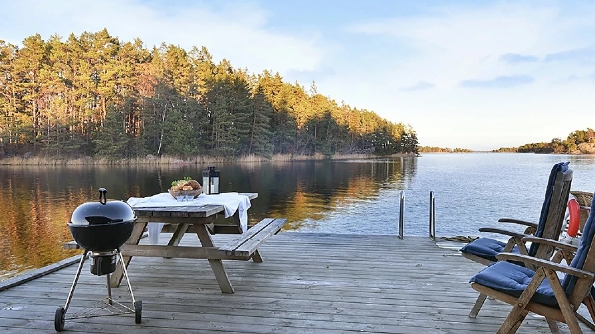 Wooden deck with chairs, table, and grill by a calm lake with forested shoreline.