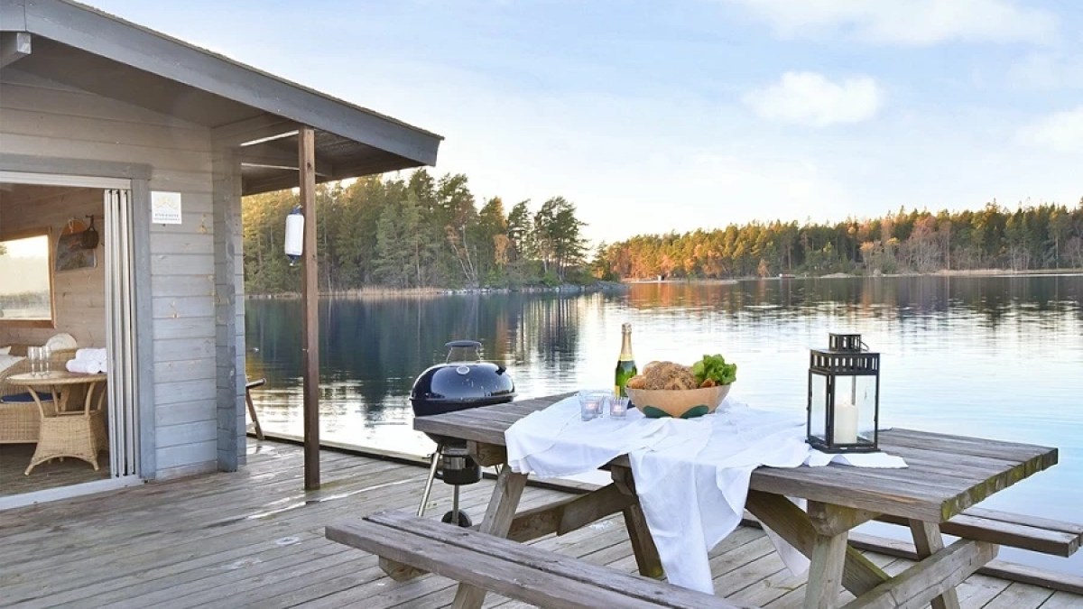 Deck with picnic table, grill, and lake view, surrounded by trees and blue sky.