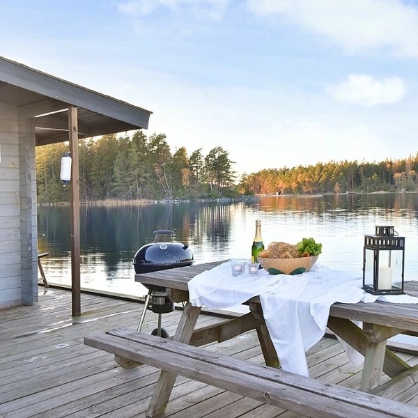 Deck with picnic table, grill, and lake view, surrounded by trees and blue sky.
