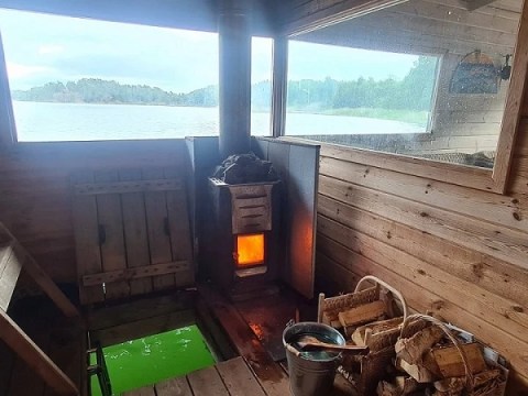 Wooden sauna with a burning stove, window view of lake.