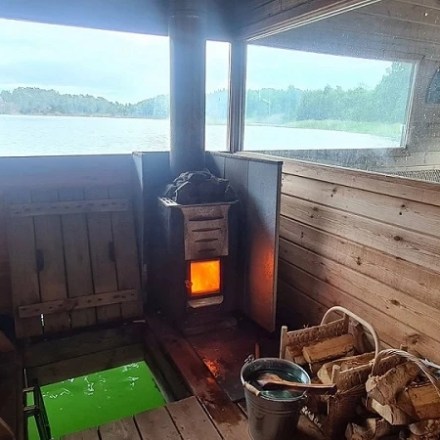 Wooden sauna with a burning stove, window view of lake.