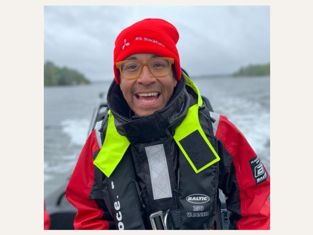 Person smiling on a boat wearing a red hat and life jacket on a cloudy day.