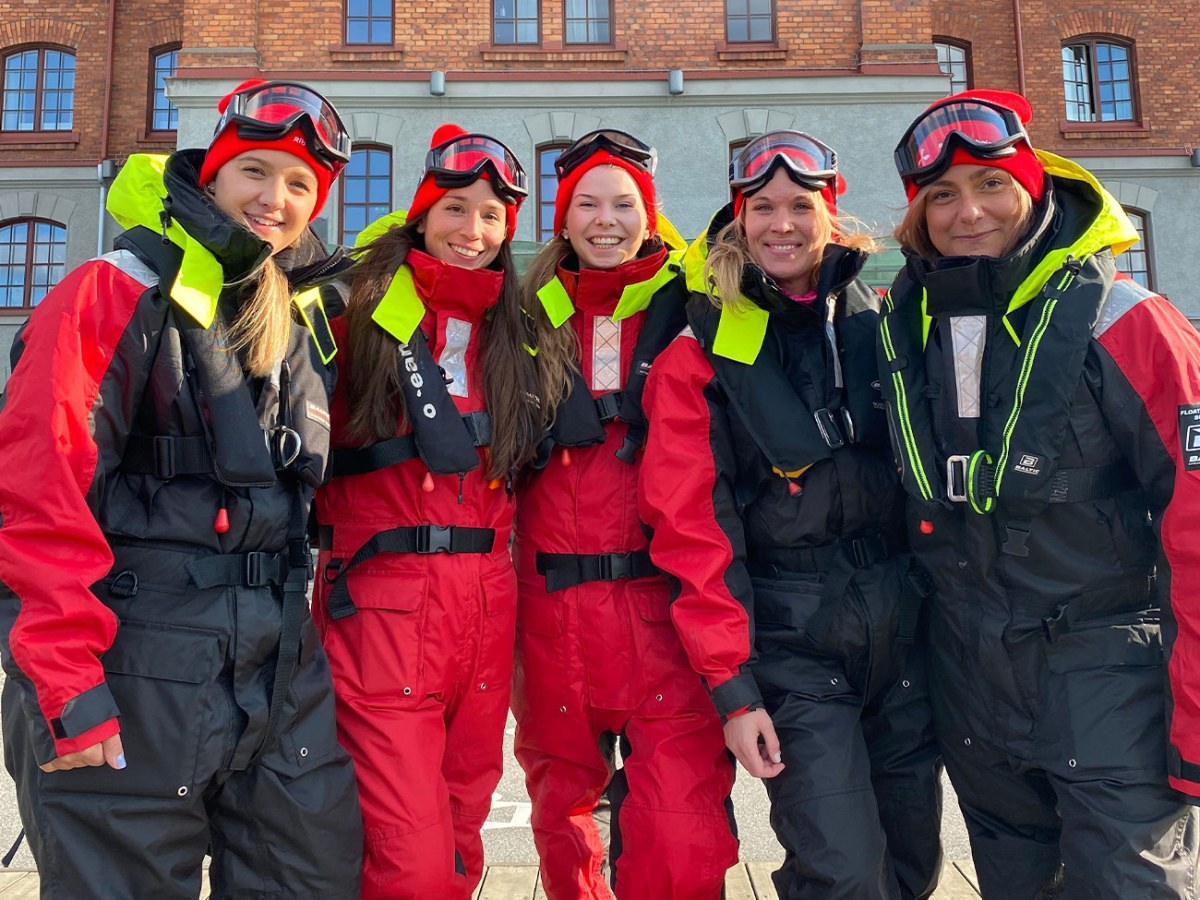 Five people in red cold-weather gear stand smiling in front of a brick building.
