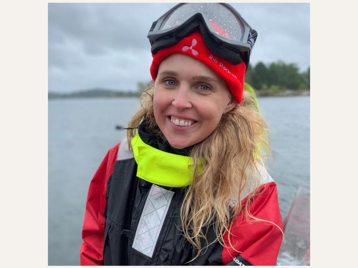 Person in a red jacket and beanie smiling by the water on a cloudy day.