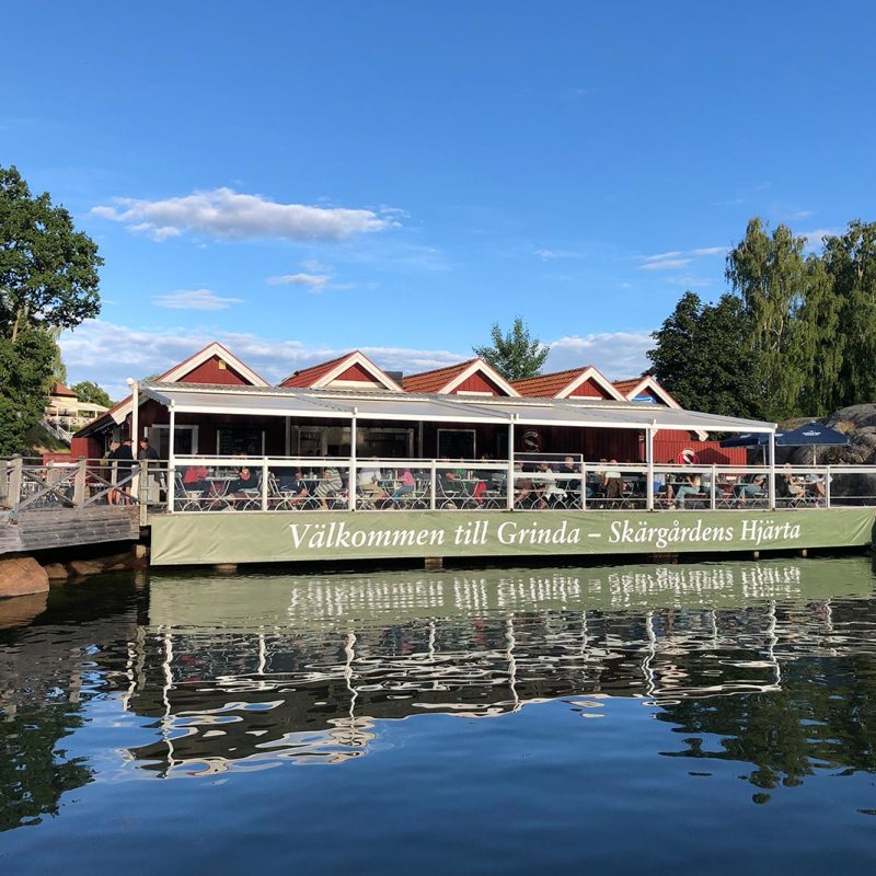 Lakeside restaurant with red buildings and outdoor seating in a green, wooded area.