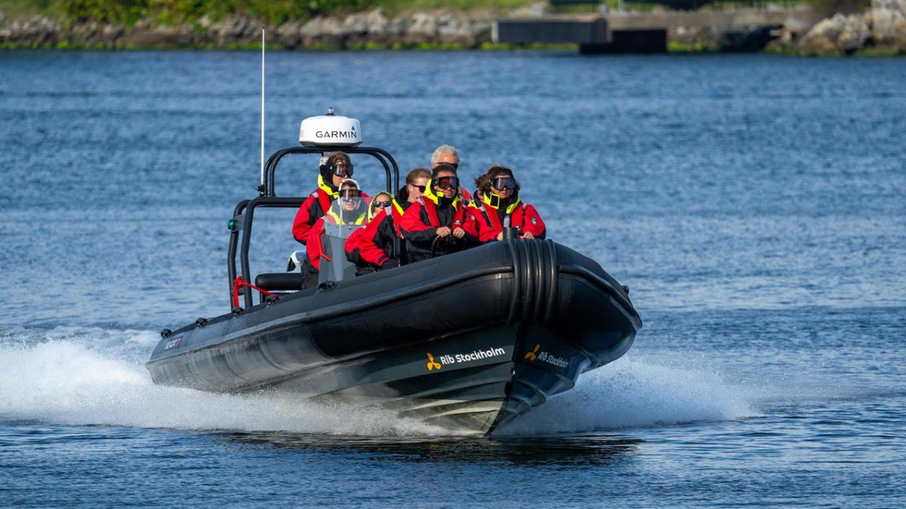 People in red jackets on a black speedboat moving fast on a river.