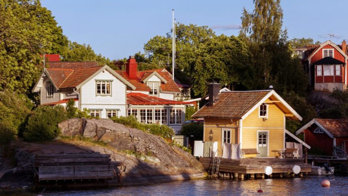 Coastal houses in a scenic landscape with trees and rocks by the water.